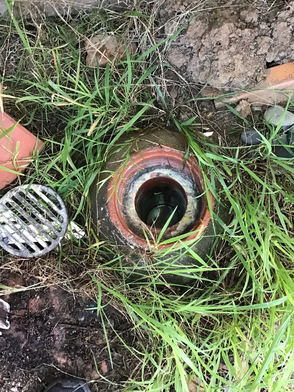 Smelly Drains Sydney - a gully in the grass with its grate lifted and grease caked around the inside in South Penrith