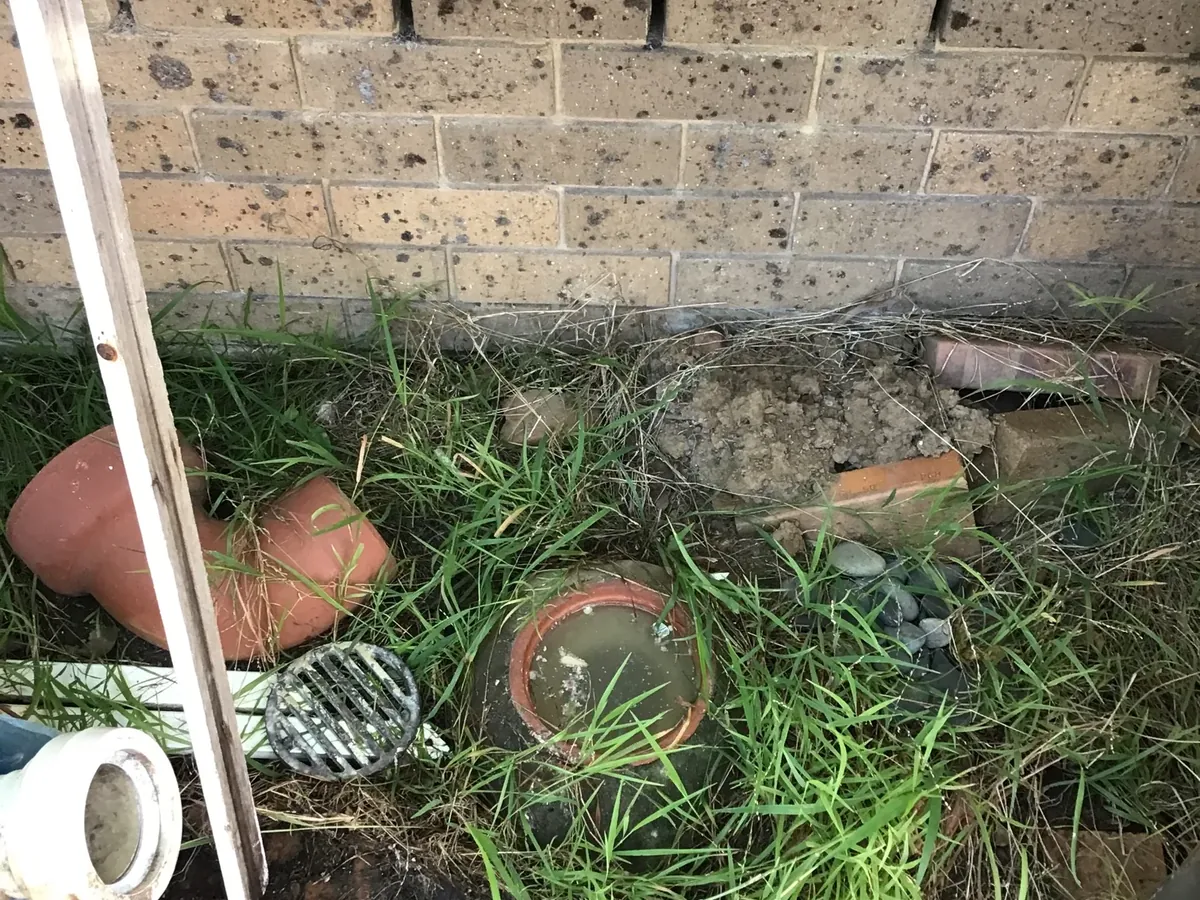 Old clay bend and a lifted grate beside a gully full of dirty water in South Penrith