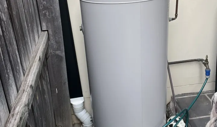 Grey electric hot water tank on a paver between a timber fence and a rendered wall in Macquarie Fields