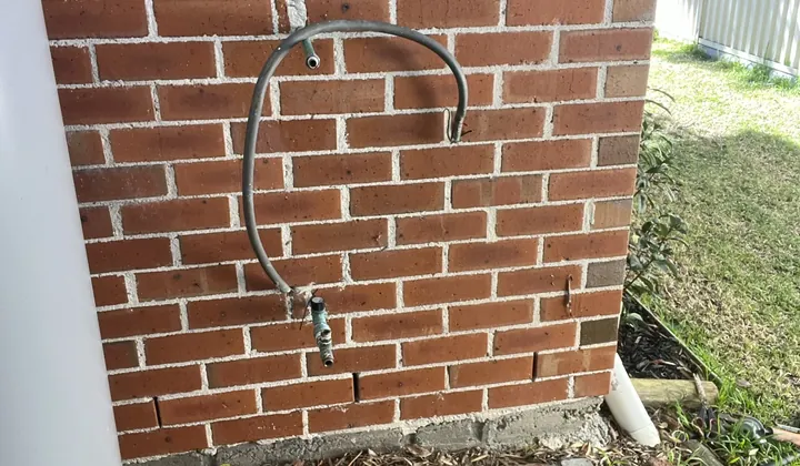 Braided water connection on the brick wall beside an old electric hot water tank in Caringbah South