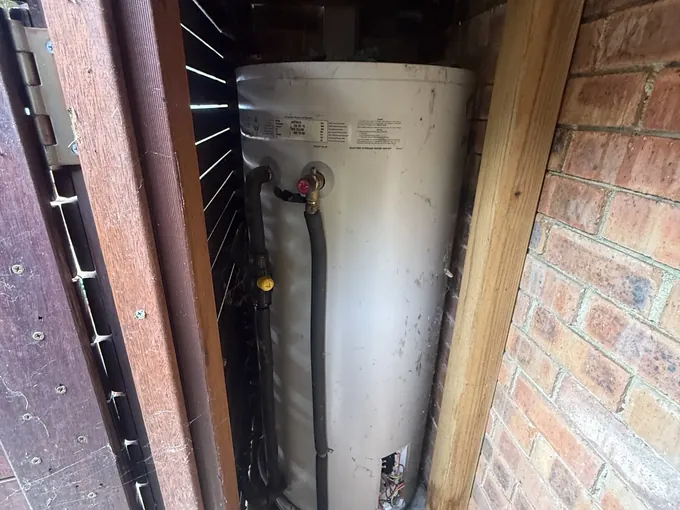 Electric hot water tank inside a timber enclosure against a brick wall in Cremorne