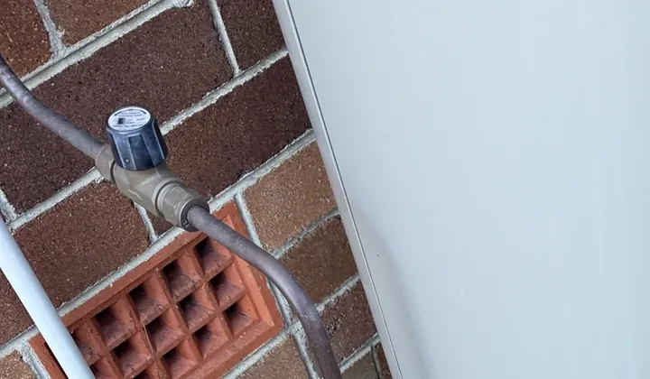 Blue-capped valve on the copper water line next to a storage tank and brick vent in Riverwood