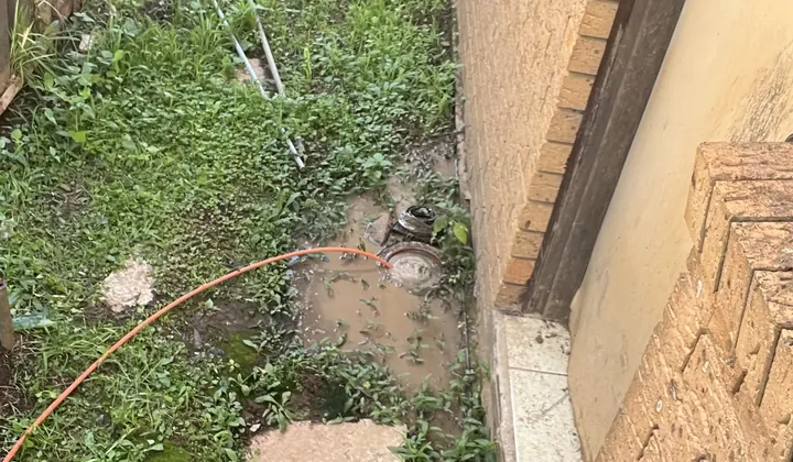 Muddy water pooled around an opened drain in a grassy side passage in Rosemeadow