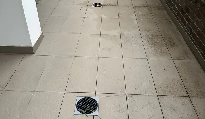 Tiled courtyard with two round floor grates and wet patches in Warwick Farm