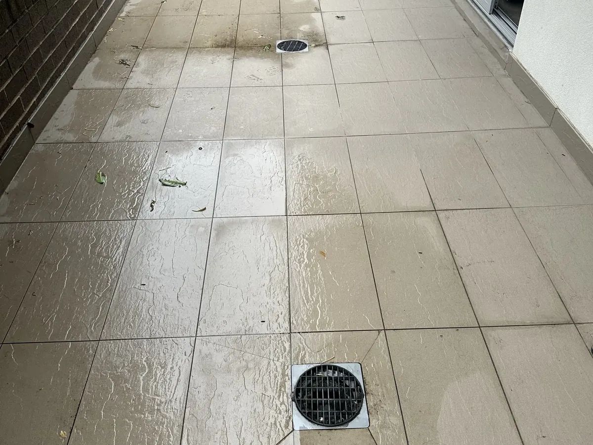 Water left sitting on a tiled courtyard around its floor drains after rain in Warwick Farm
