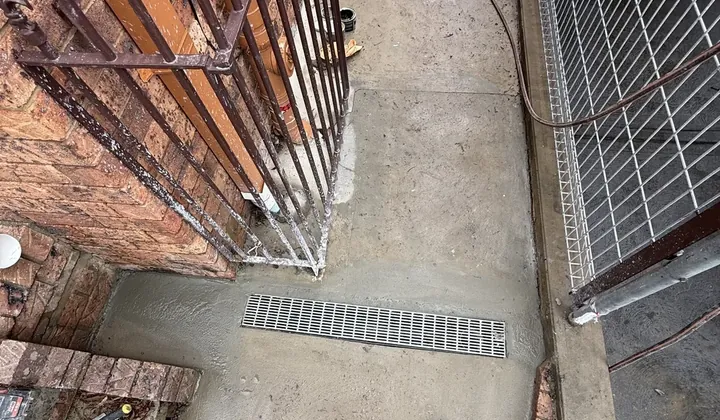 New strip drain grate set in fresh concrete across a side path in Cromer