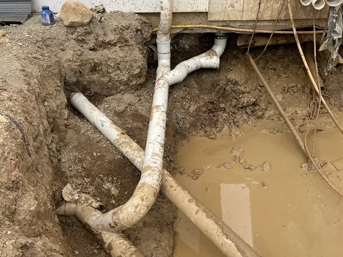 New storm water pipes and downpipe junctions laid in an open trench beside a new house in Wilton