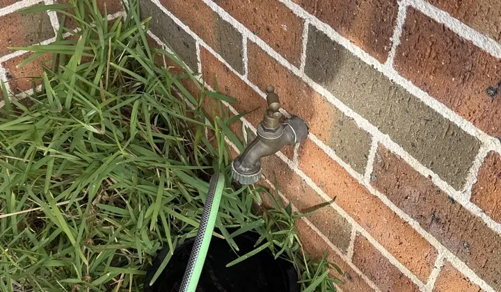 Brass garden tap with a hose attached on a brick wall in South Wentworthville