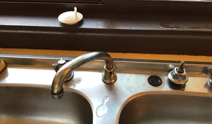 Old kitchen taps and swivel spout on a stainless sink below a window in Greenfield Park