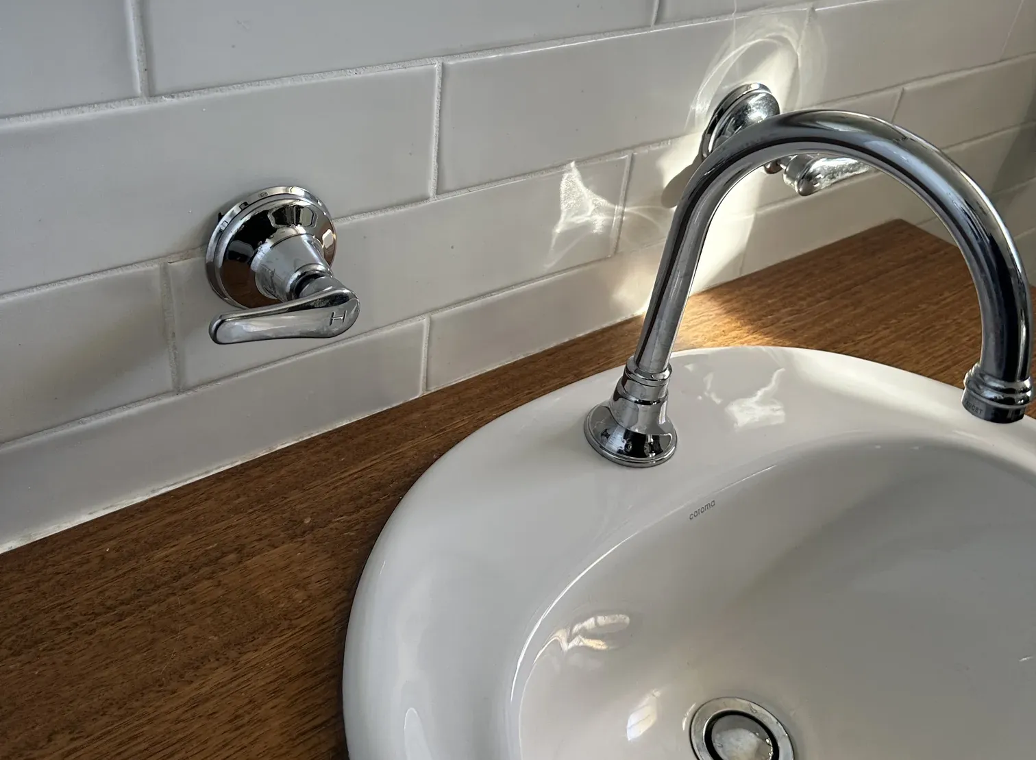 Lever wall tap and chrome spout over a white basin on a timber bench in Greenacre