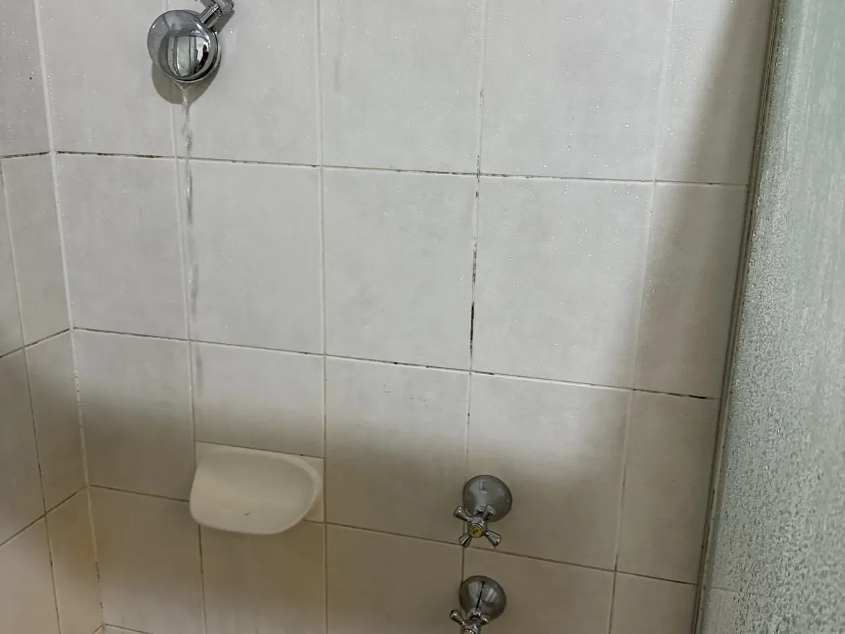 Water running down the tiles from a shower arm, above the shower taps, in Bankstown