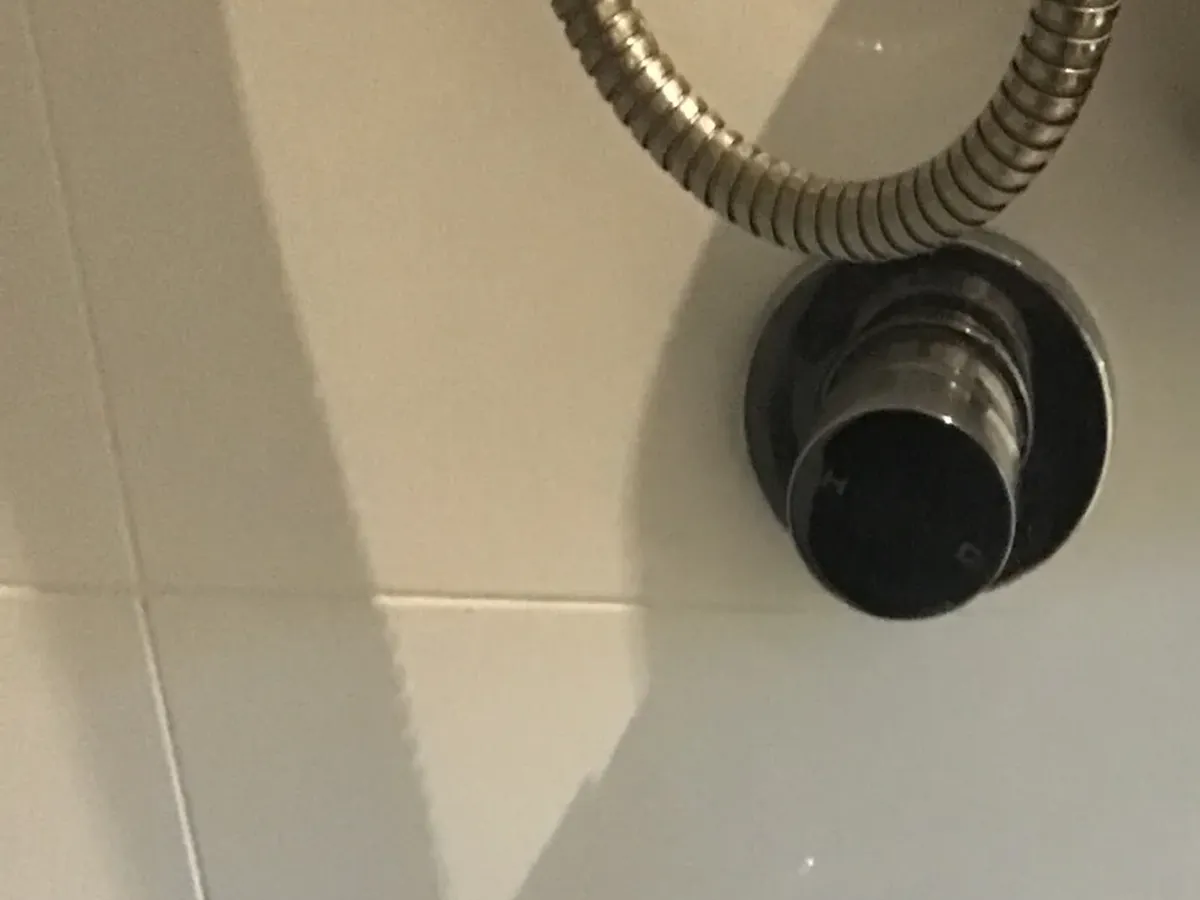 Shower mixer and hand shower hose on a white tiled wall in Campsie