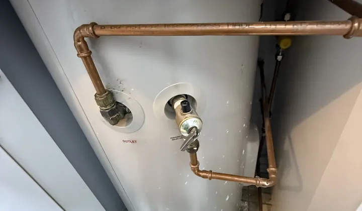 Relief valve and copper pipes on the side of a storage tank inside a cupboard in Bexley
