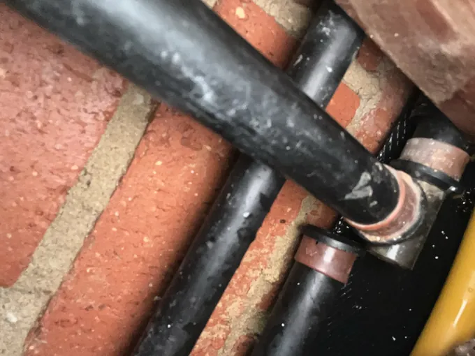 Lagged and copper hot water pipes running across a brick wall in Oran Park