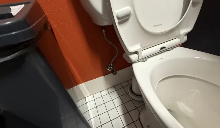 Toilet with a braided hose and stop tap in a business washroom in Artarmon