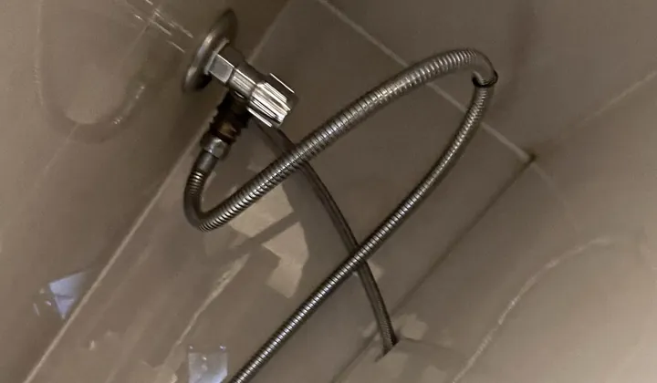 Chrome stop tap and braided hose running into the side of a toilet in Earlwood