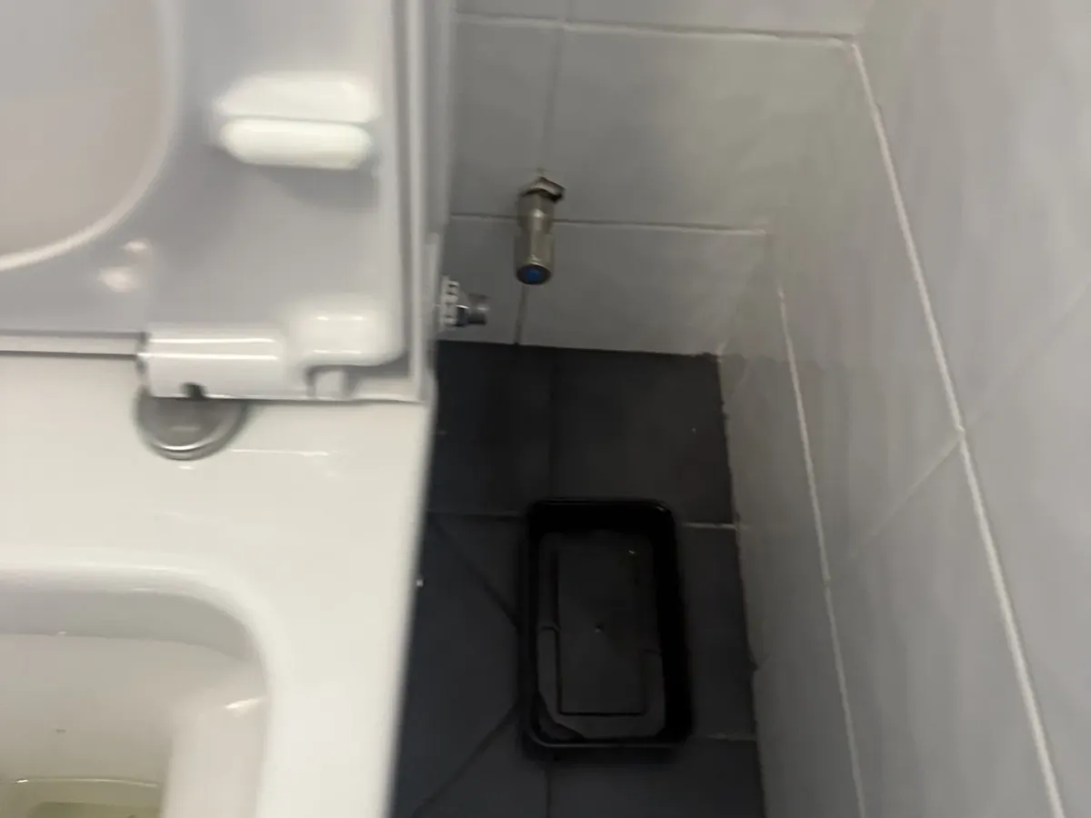 Stop tap on the tiled wall beside a toilet, with a tray on the floor below, in Panania