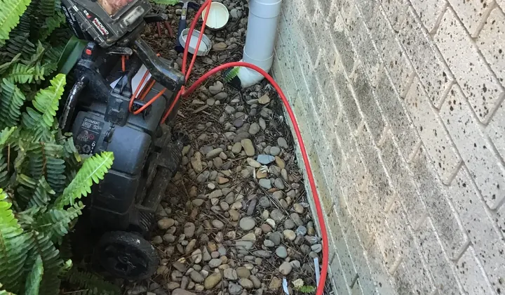 Jet blaster hose and drain camera set up at a drain opening beside a brick wall in Baulkham Hills