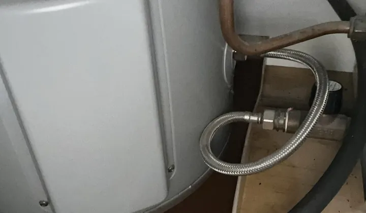 Braided hose connection at the base of a hot water tank sitting in a tray in Randwick