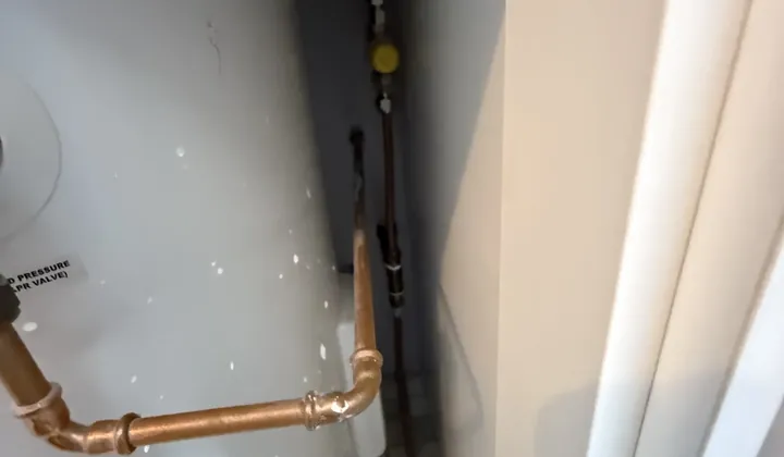 Hot water tank in a tight cupboard with water marks on its side and copper pipework