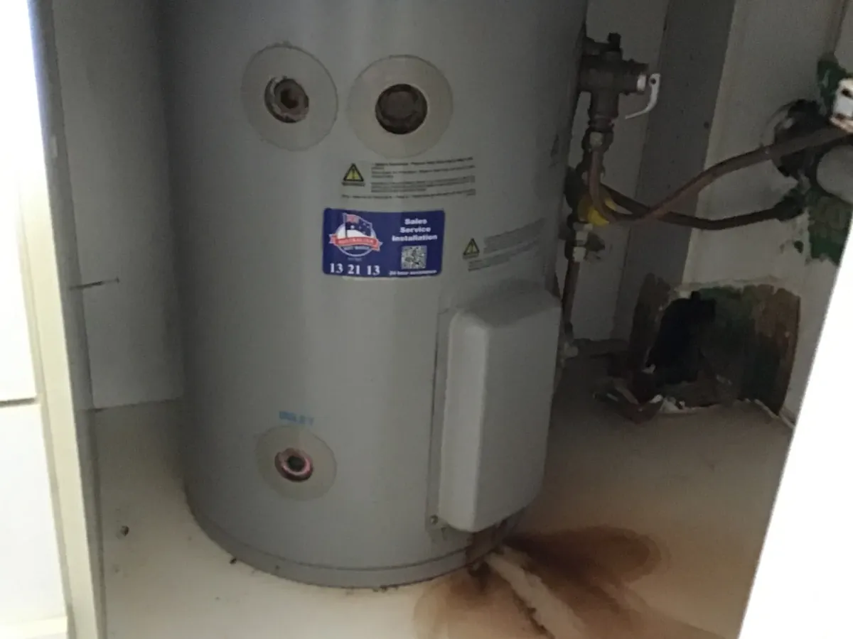 Rust-coloured water stain spreading from the base of an electric hot water tank in a cupboard in Campsie