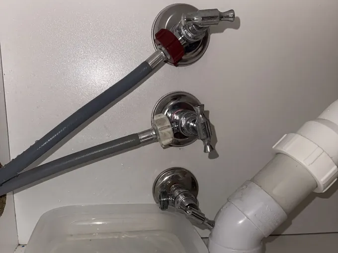 Grey inlet hoses connected to chrome washing machine taps above a drip tray in Harrington Park