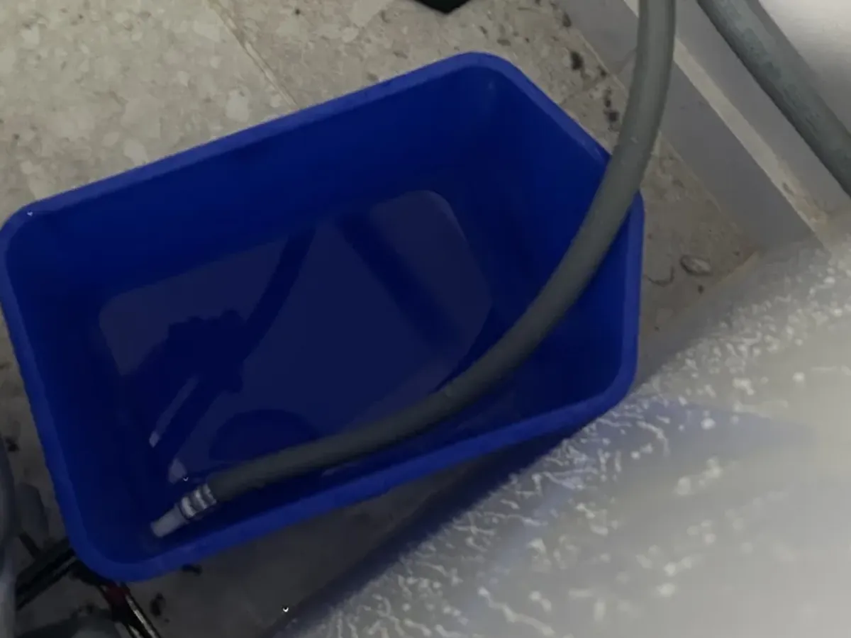 Washing machine hose laid in a blue bucket behind the machine after a hose leak in Jannali