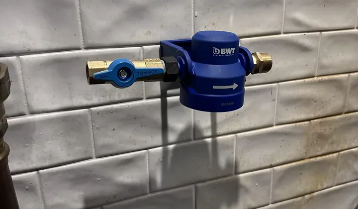 New water filter head and brass isolation valve fixed to a tiled wall, before the cartridge goes on