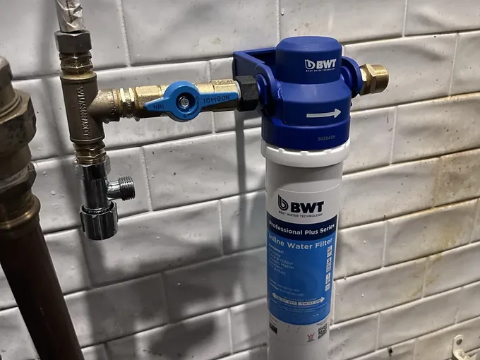New cartridge fitted to a new filter head beside a brass isolation valve on a tiled wall