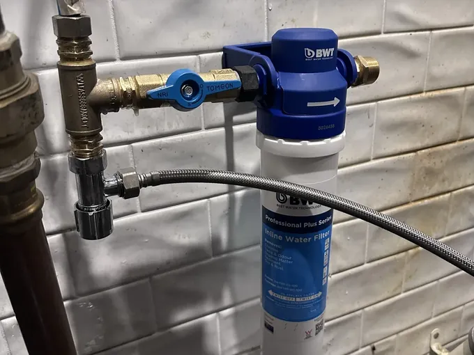 Braided hose connected to the tee on the water line beside a new inline filter with its cartridge in place
