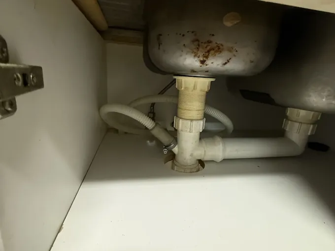 Waste pipes and hoses under a double kitchen sink in Maianbar