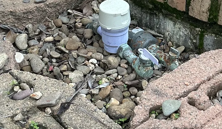 Water meter and its meter tap among river pebbles beside a brick garden edge in Rouse Hill