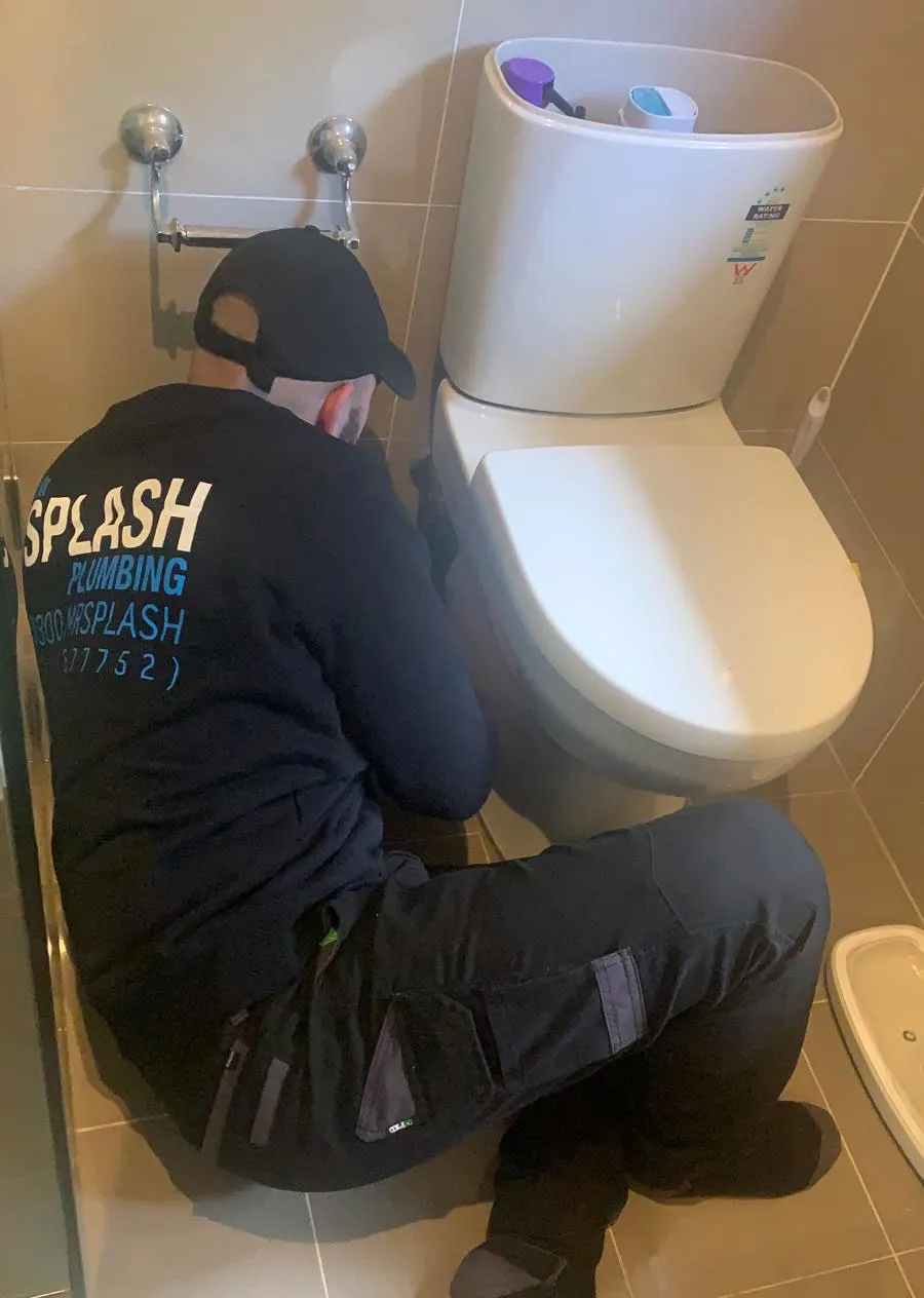 Mr Splash plumber repairing a toilet in a tiled bathroom