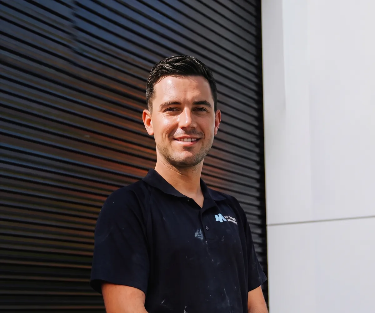 Friendly plumber in a navy polo in front of a timber-slat wall